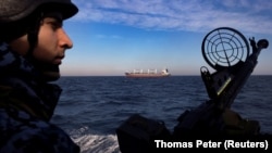 A member of Ukraine's coast guard mans a gun on a patrol boat as a cargo ship passes by in the Black Sea in February 2024. 