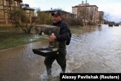 Мужчина несет клетку с попугаем, идя по затопленной после шторма улице в Евпатории, Крым, 27 ноября 2023 года